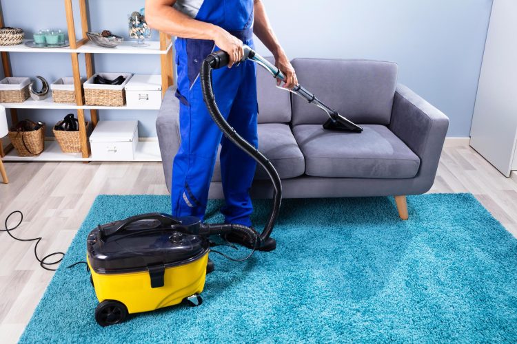 Cleaner using deep-clean extraction machine on carpet and sofa in London home